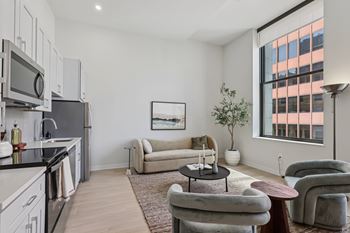 A modern kitchen with a large window and a living room area with a couch and chairs.